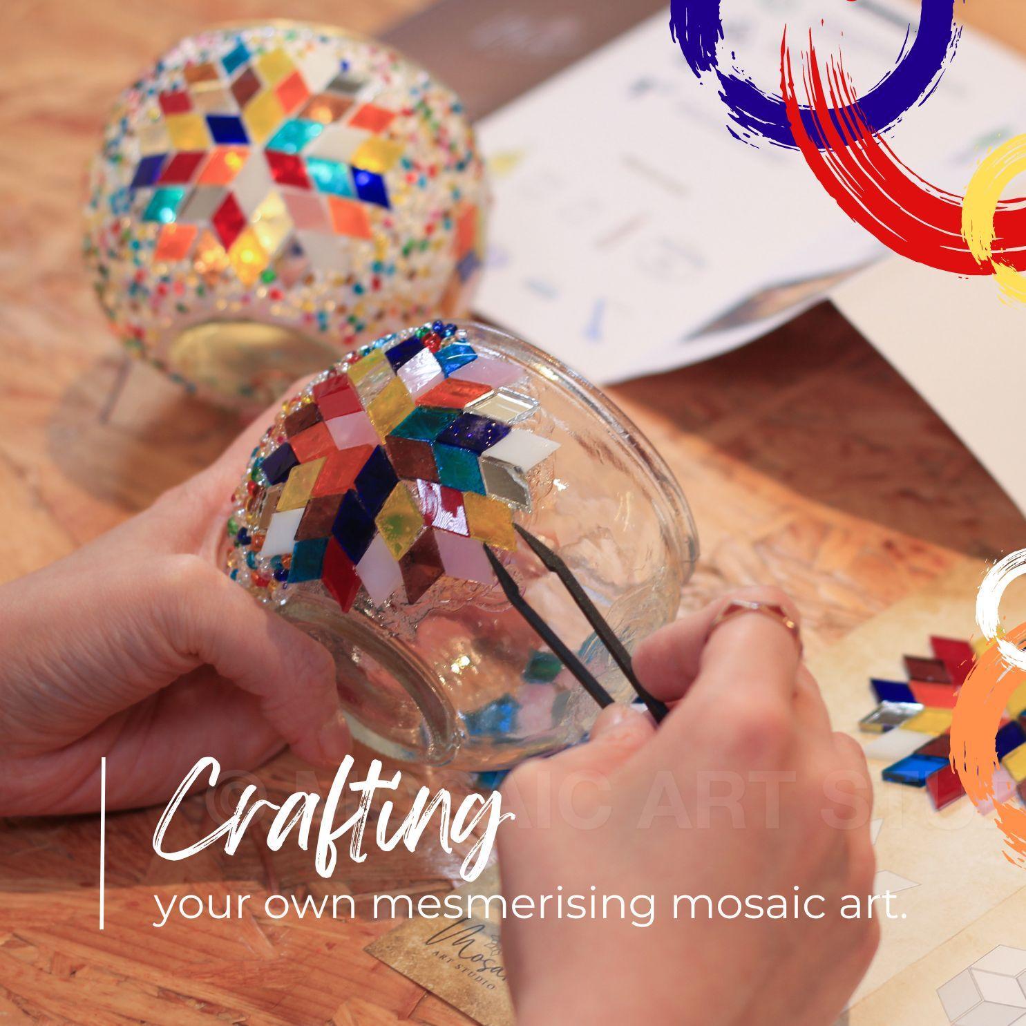 Hands crafting colorful mosaic pattern on glass candle holder using tweezers on wooden table