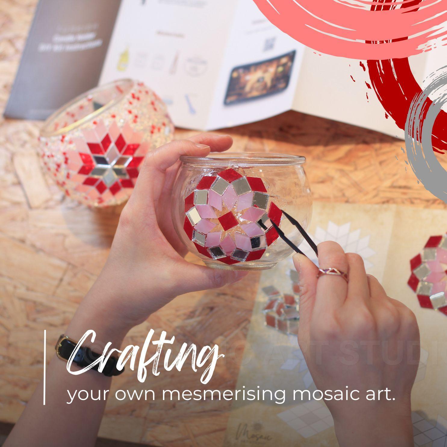 Hand crafting a mosaic glass candle holder with red and pink tiles using tweezers on wooden table