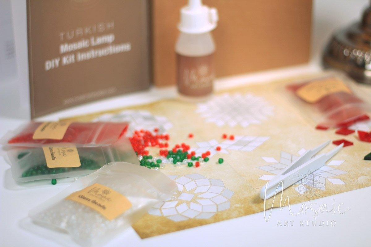 Christmas mosaic candle holder DIY kit with colored beads, glue bottle, and tweezers on patterned paper