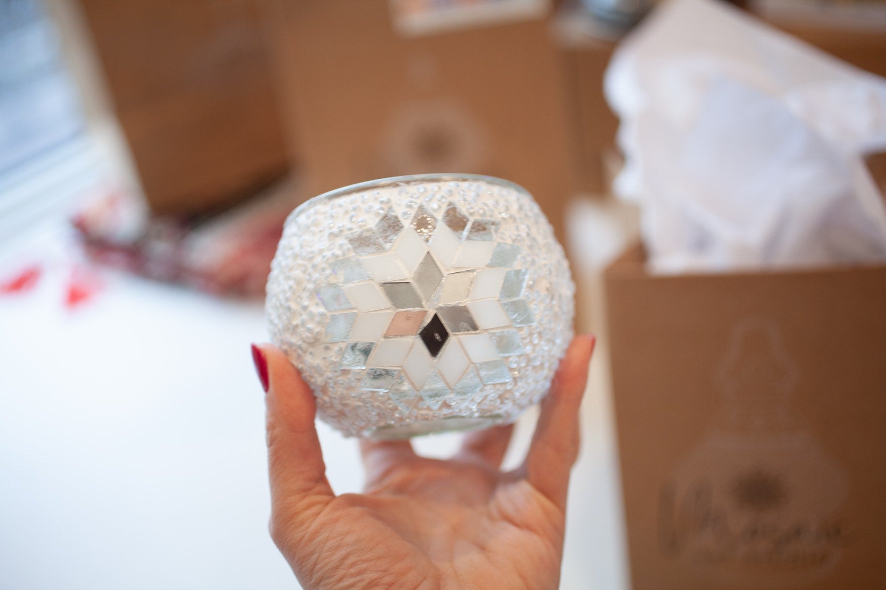 A finished mosaic globe held up beside its gift bag and tissue paper