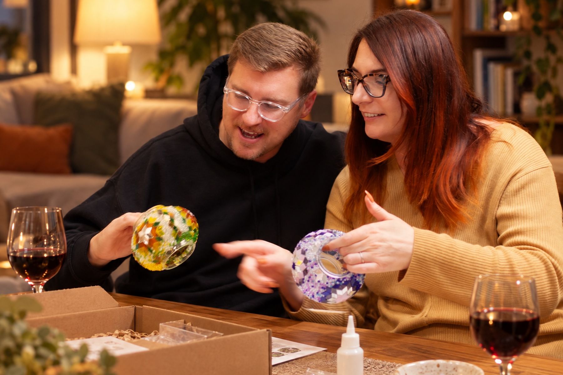 A couple at home laughing as they hold up the mosaic globes they made