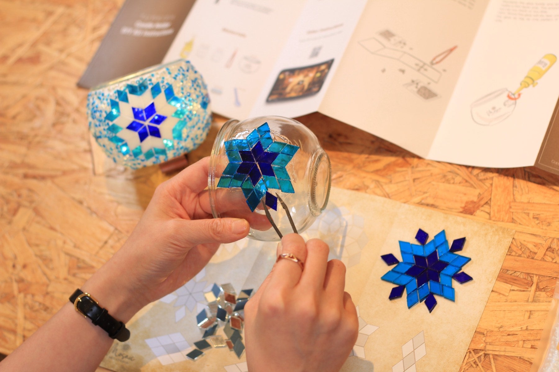 Hands placing the first glass pieces with the kit instructions open