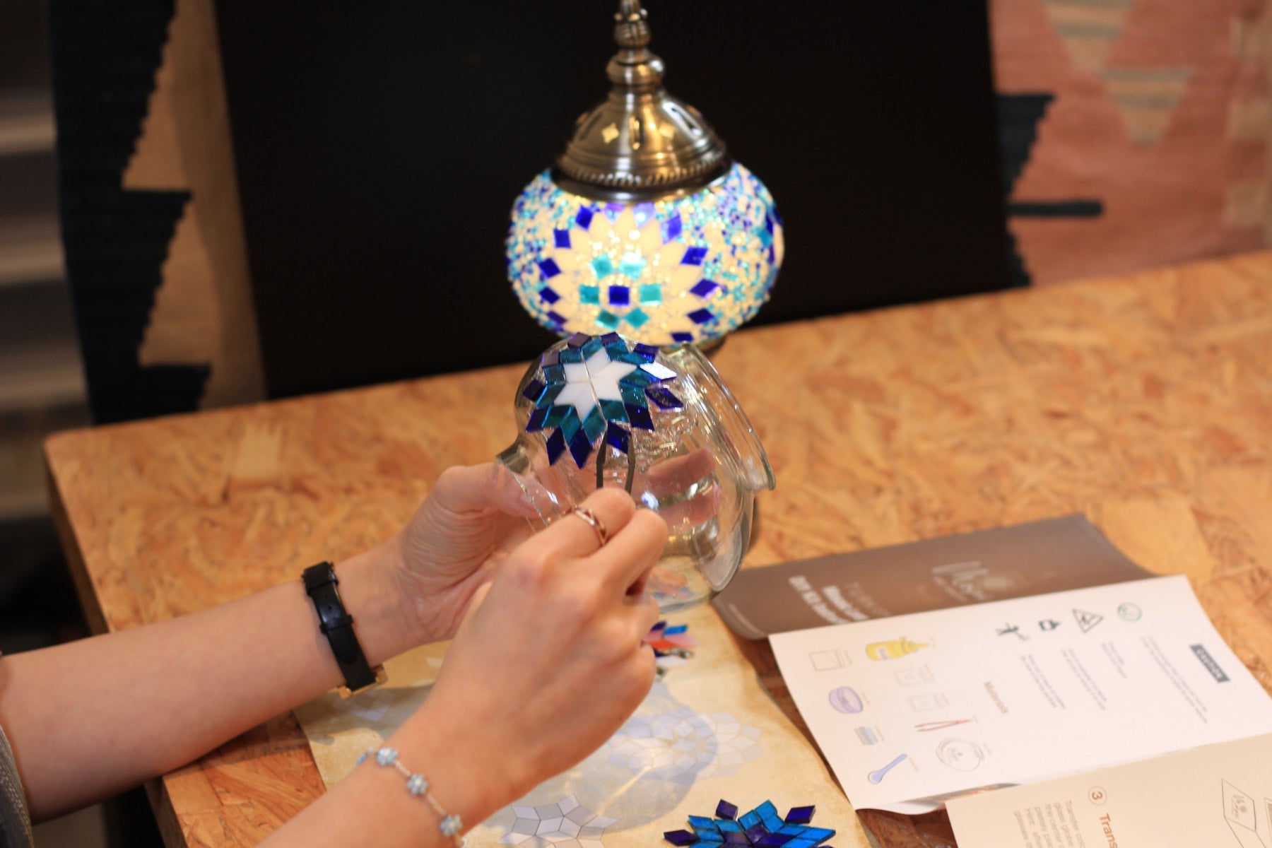 A finished blue mosaic lamp glowing beside the kit instructions