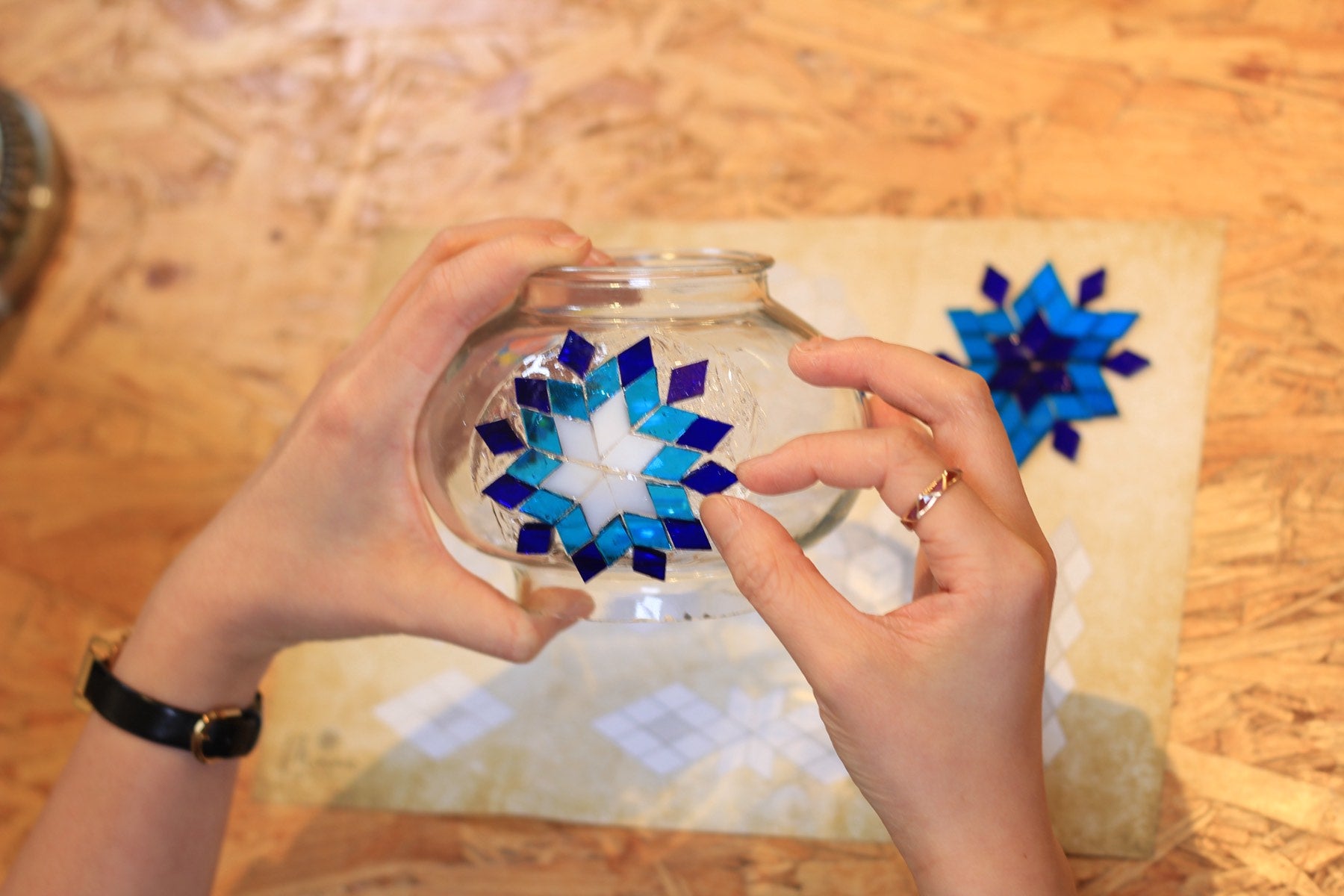 Hands pressing blue glass pieces into a star on a glass globe