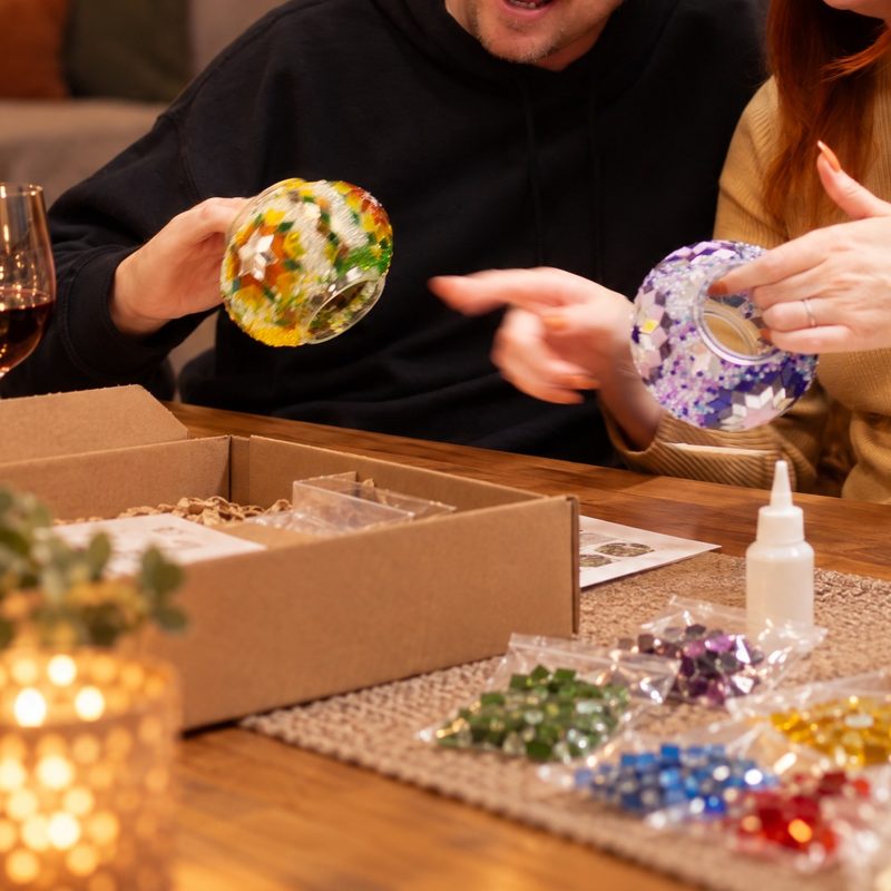 A couple holding up their finished mosaic globes over the open kit box at home